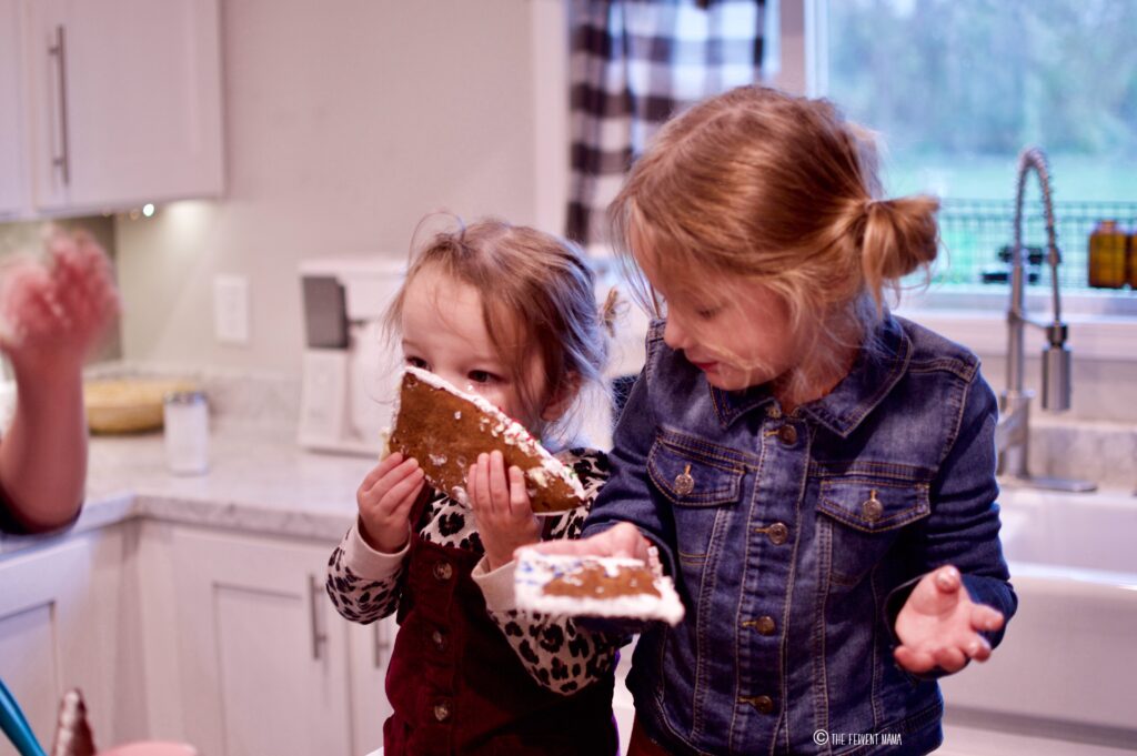 Two young girls eating a gingerbread house.