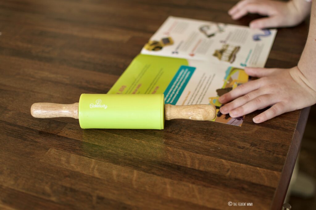 Baketivity themed rolling pin and their educational book on a counter with child hands.