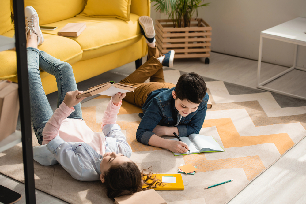 siblings laying on the floor completing schoolwork together in their homeschool.