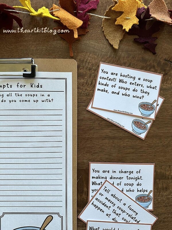 Soup-Writing-Prompts-The-Art-Kit-6 Colorful autumn felt leaves creating a cozy homeschool atmosphere with soup-themed educational cards and printable worksheet for kids' activities.