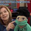 A woman with red hair and a puppet wearing a green face mask and scrubs participating in a virtual preschool session with children.