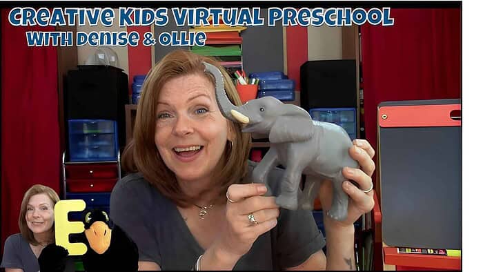 A colorful classroom scene featuring a smiling woman holding a gray elephant toy, with educational materials and storage bins in the background, promoting creative kids virtual preschool.