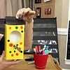 Woman demonstrating a colorful homemade birdhouse craft project for homeschooling activities.