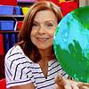 Homeschool teacher holding a colorful painted paper plate in a classroom setting.