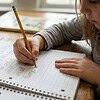 Young girl practicing handwriting in a notebook for homeschooling, focusing on alphabet and letter formation.