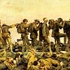 A soldier helping a wounded comrade during a military training exercise, with other soldiers in the background.