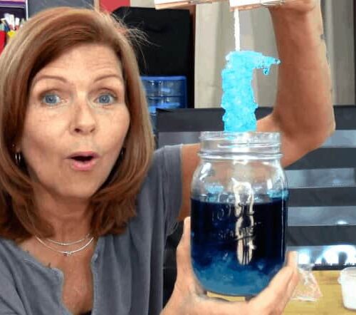 Woman demonstrating a science experiment with a blue substance in a jar, showcasing homeschooling science activities.