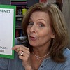 Woman holding a list of 10 weekly homeschool themes including fairy tales, life cycles, birds, spring, pond life, plants, safari animals, earth day, mice, and underground life.