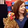Woman engaging with two puppet chickens in a colorful classroom setting, promoting homeschooling activities.