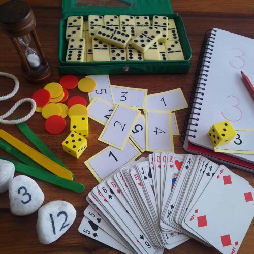 Board game setup with dominoes, dice, playing cards, and scorekeeping notes on a wooden table, ideal for family or educational activities.