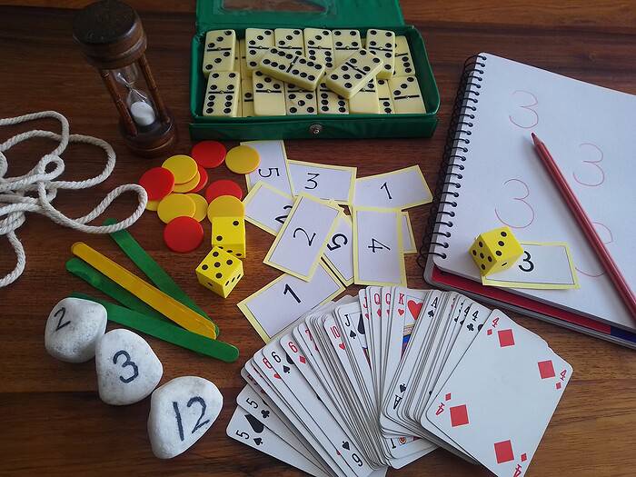 Exif_JPEG_420 Board game setup with dominoes, dice, playing cards, and scorekeeping notes on a wooden table, ideal for family or educational activities.
