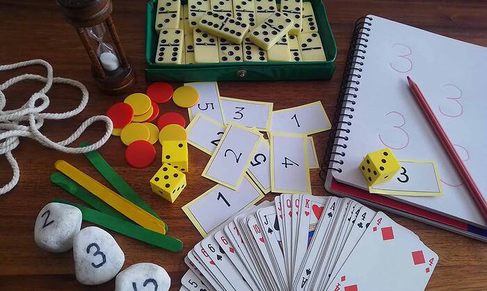 Exif_JPEG_420 Educational game setup with dominoes, playing cards, dice, and scorecards for homeschooling activities.