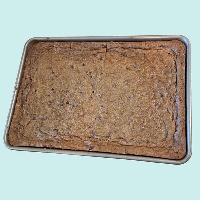 blondies bars (2000 x 2000 px) (2) Homemade chocolate chip cookie bar in a metal baking tray on a light blue background.