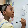 Young Girl Solving Math Problems on Whiteboard Young girl with braided hair solving math problems on a whiteboard in a classroom setting, focusing on her learning process.