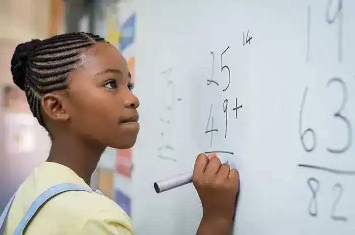 Young Girl Solving Math Problems on Whiteboard Young girl with braided hair solving math problems on a whiteboard in a classroom setting, focusing on her learning process.