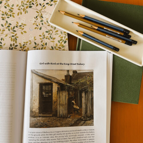 Young student workspace with an open book, pencils in a tray, and notebooks on a wooden desk, evoking homeschool learning environment.