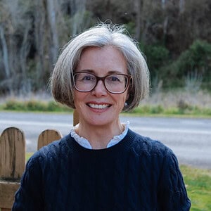 cropped-The-Gentle-Edit_portraits-16-2-1.jpg Smiling woman with glasses and gray hair outdoors, representing homeschooling resources and education.