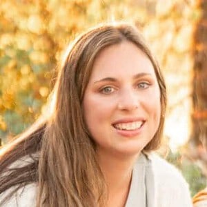 Smiling young woman outdoors in autumn with fall foliage background, representing homeschooling and outdoor learning.