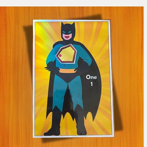 Colorful Batman card with cape and shield design, bright yellow radial background, labeled One 1, suitable for educational activities and homeschool projects.